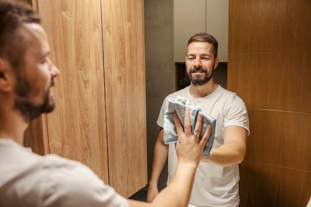 Un hombre aseado está limpiando el espejo en un cuarto de baño.