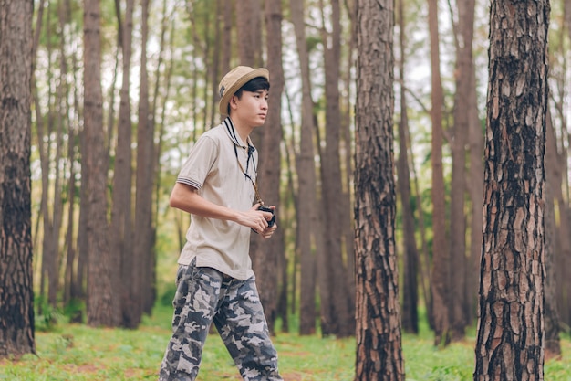El hombre de Asia usa camisa, sombrero y pantalones de camuflaje, camina y toma fotos en el bosque