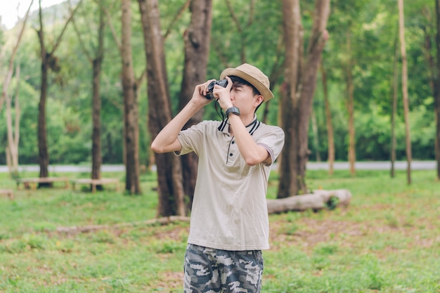 El hombre de asia usa camisa, sombrero y pantalones de camuflaje, camina y toma fotos en el bosque