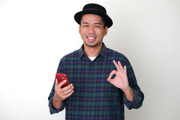 Foto hombre asiático adulto da signo de dedo ok cuando sostiene su teléfono móvil