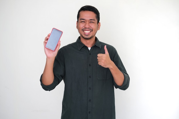 Hombre asiático adulto dando pulgar hacia arriba mientras muestra la pantalla en blanco de su teléfono móvil