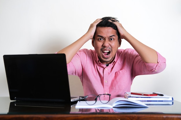 Hombre asiático adulto mostrando expresión estresada en su mesa de trabajo