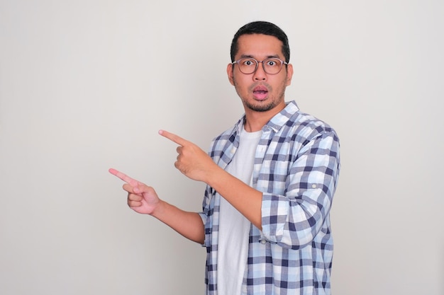 Hombre asiático adulto que muestra una expresión de asombro con ambas manos apuntando hacia el lado derecho