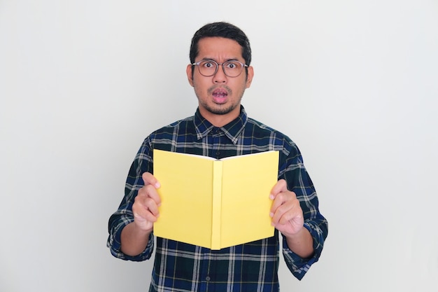 Foto hombre asiático adulto que muestra una expresión de asombro mientras sostiene un libro