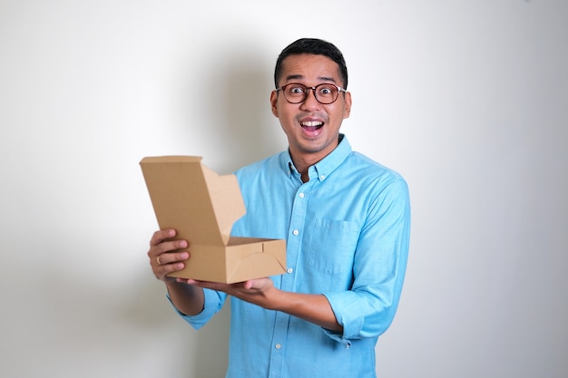 Hombre asiático adulto que muestra la expresión de la cara de sorpresa cuando abre una caja de regalo