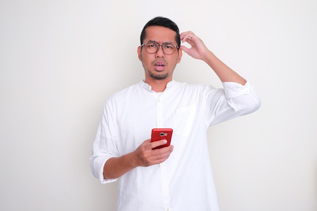 Hombre asiático adulto que muestra una expresión confusa mientras sostiene el teléfono móvil