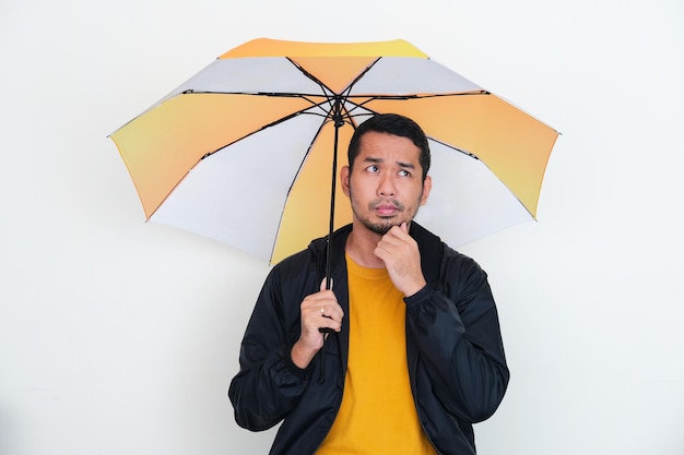 Hombre asiático adulto que muestra expresión de pensamiento mientras sostiene un paraguas