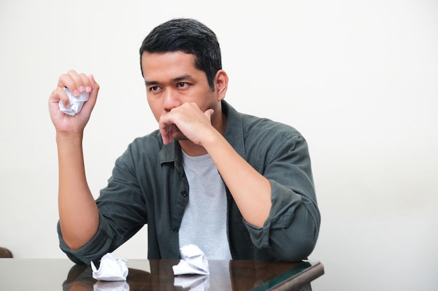 Foto hombre asiático adulto que muestra un gesto de frustración mientras aplasta un documento en papel