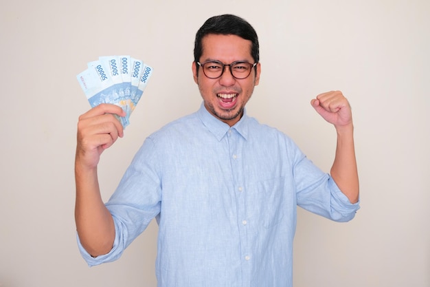 Hombre asiático adulto que muestra un gesto fuerte mientras sostiene dinero