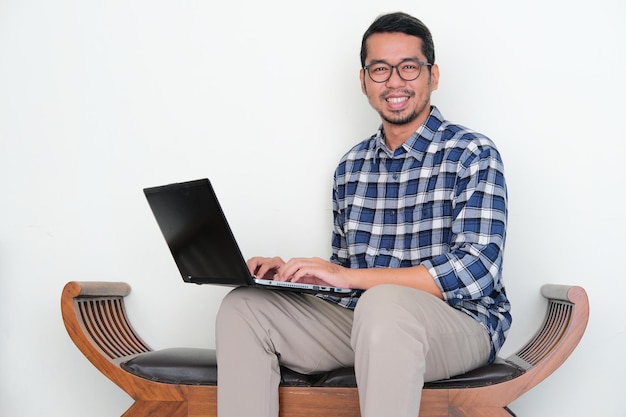 Hombre asiático adulto sentado en un banco sonriendo confiado cuando trabaja con una computadora portátil