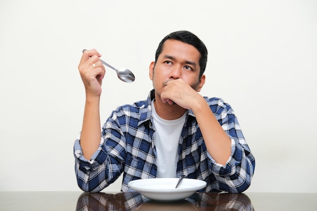 Hombre asiático adulto sentado frente a un plato vacío mientras muestra una expresión confusa