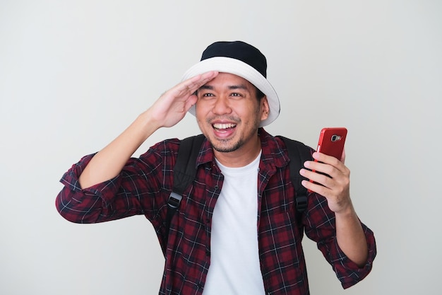 Hombre asiático adulto con sombrero de cubo y mochila sonriendo feliz cuando mira hacia adelante, concepto de viaje