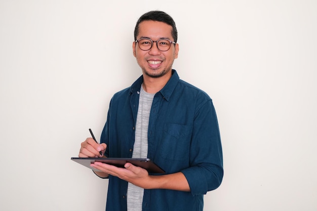 Hombre asiático adulto sonriendo a la cámara cuando trabaja con un dispositivo de tableta móvil