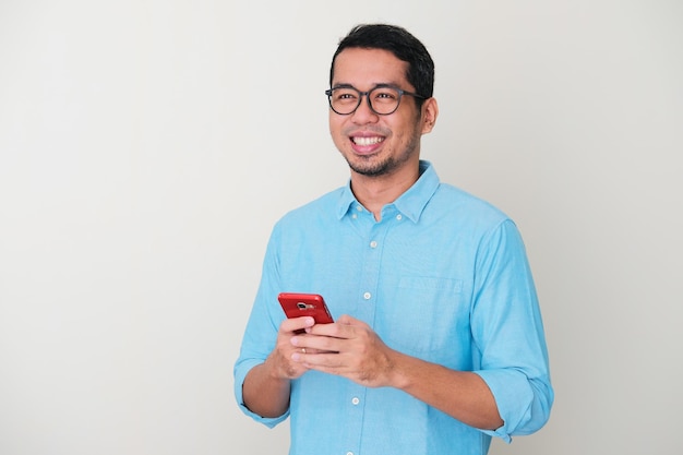 Hombre asiático adulto sonriendo confianza mientras sostiene el teléfono móvil