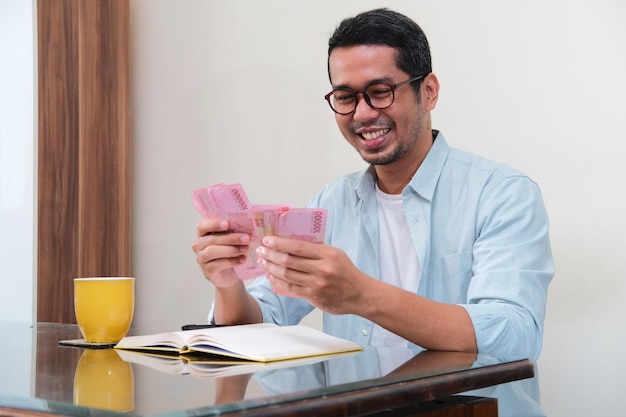 Hombre asiático adulto sonriendo feliz al contar el dinero que gana