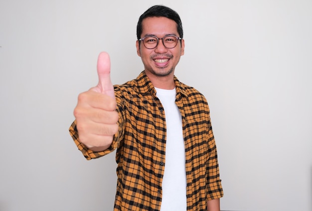 Hombre asiático adulto sonriendo feliz a la cámara y levantando el pulgar