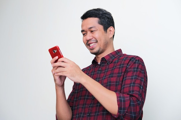 Hombre asiático adulto sonriendo feliz cuando mira su teléfono móvil