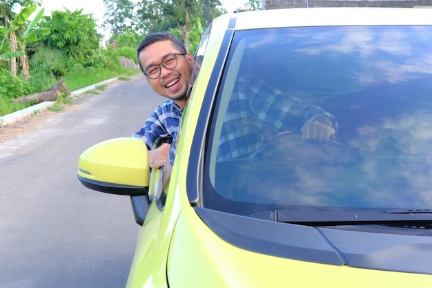 Hombre asiático adulto sonriendo feliz mientras mira afuera desde el interior de su auto