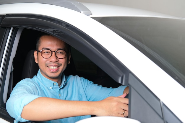 Hombre asiático adulto sonriendo feliz mientras mira a la cámara desde el interior de su coche