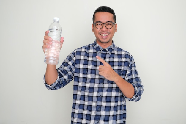 Hombre asiático adulto sonriendo feliz mientras señala la botella de agua potable que sostiene