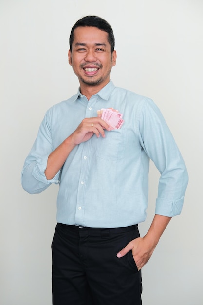 Hombre asiático adulto sonriendo mientras pone dinero dentro del bolsillo de su camisa