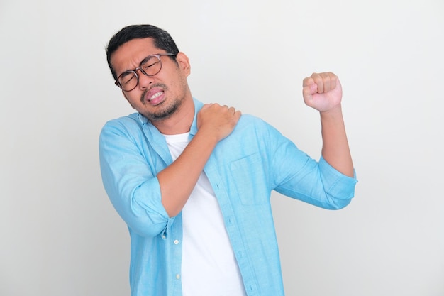 Hombre asiático adulto tocando su hombro izquierdo con expresión de dolor