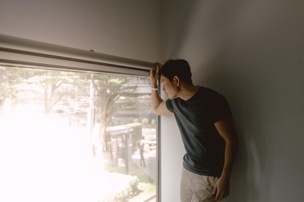 Hombre asiático apoyado en una pared mira por la ventana