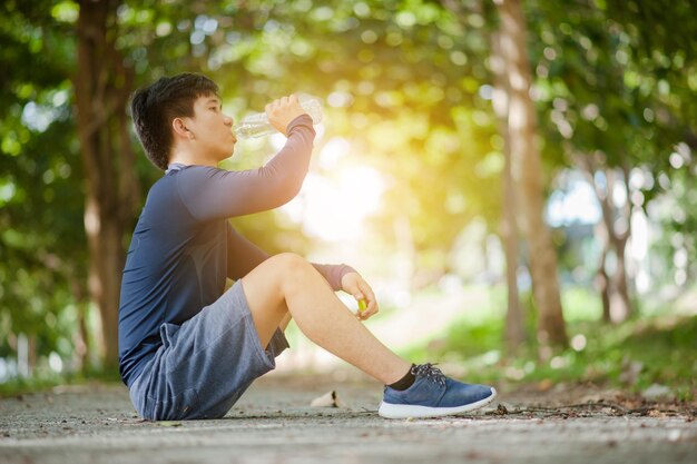 Hombre asiático bebe agua de una botella después de correr en el parque