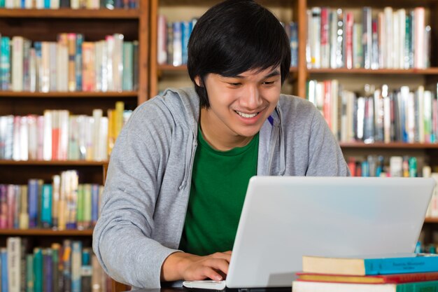 Hombre asiático en biblioteca con laptop