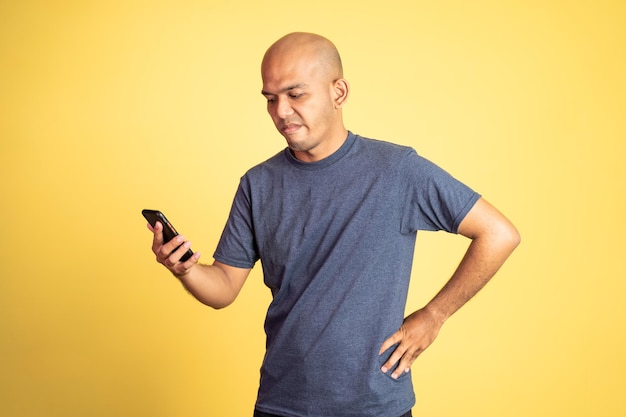 Hombre asiático calvo enojado mientras mira el teléfono móvil