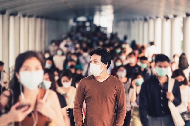 Hombre asiático caminando y de pie entre la multitud de gente de negocios irreconocible borrosa