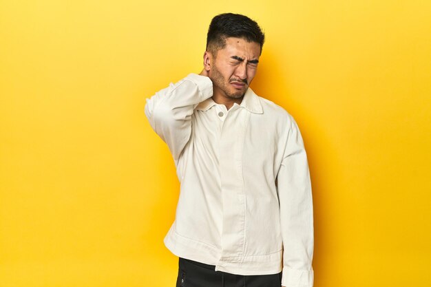 Hombre asiático con camisa blanca crujiente en un estudio amarillo sufriendo dolor de cuello debido al estilo de vida sedentario