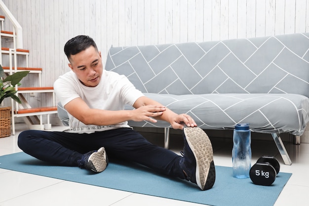 Hombre asiático en camisa blanca sobre alfombra azul hacer ejercicios de estiramiento en casa