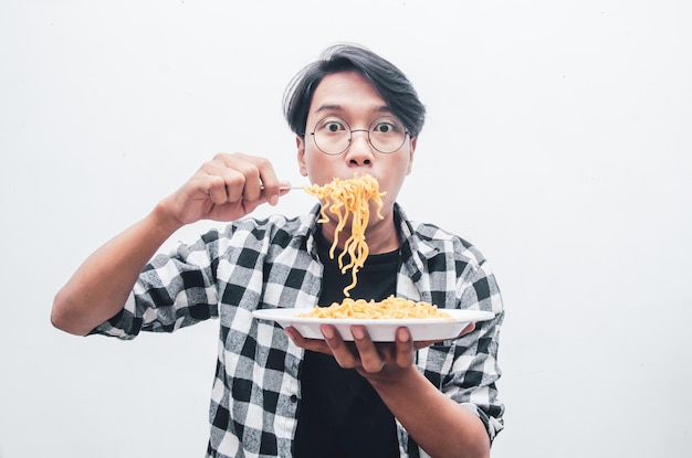 Hombre asiático con camisa casual come fideos instantáneos usando un tenedor con avidez