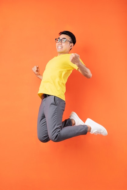 Hombre asiático en camiseta amarilla saltando sobre pared naranja