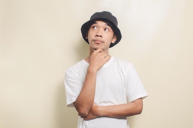 Hombre asiático con camiseta blanca brillante con sombrero negro pensando en ideas sobre un fondo aislado