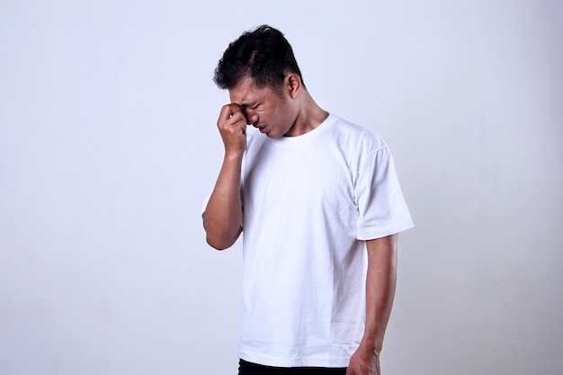 Hombre asiático en camiseta blanca con expresión sosteniendo frente aislado sobre un fondo blanco.