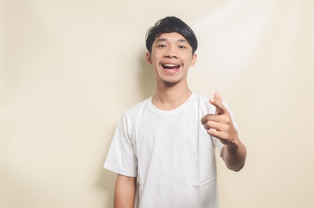 Hombre asiático con camiseta blanca feliz mientras señala con la mano hacia adelante un fondo aislado