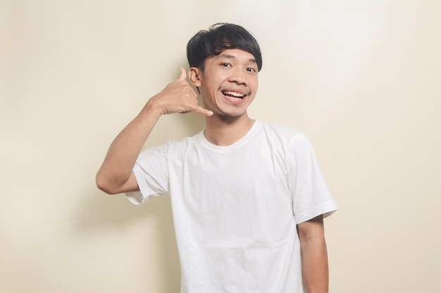 Hombre asiático con camiseta blanca con gesto de teléfono con las manos en un fondo aislado