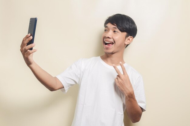 Hombre asiático con camiseta blanca con gesto tomando fotos usando un teléfono inteligente en un fondo aislado