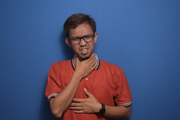 Hombre asiático con camiseta casual naranja tocando dolor de cuello dolor de garganta por gripe e infección