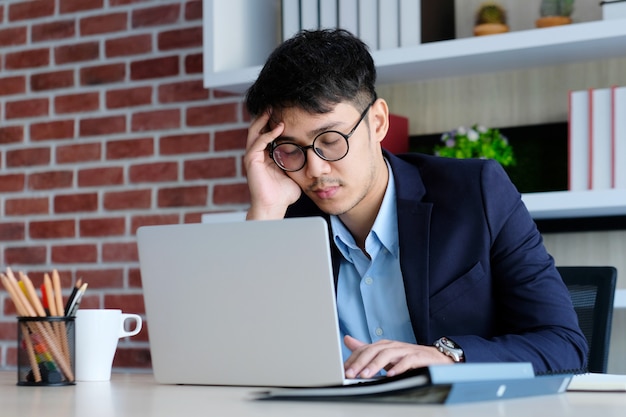 Hombre asiático cansado que duerme en el escritorio de oficina