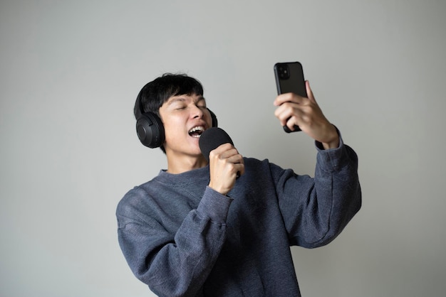 Hombre asiático cantando escuchando música en el teléfono inteligente usando auriculares Gesto feliz