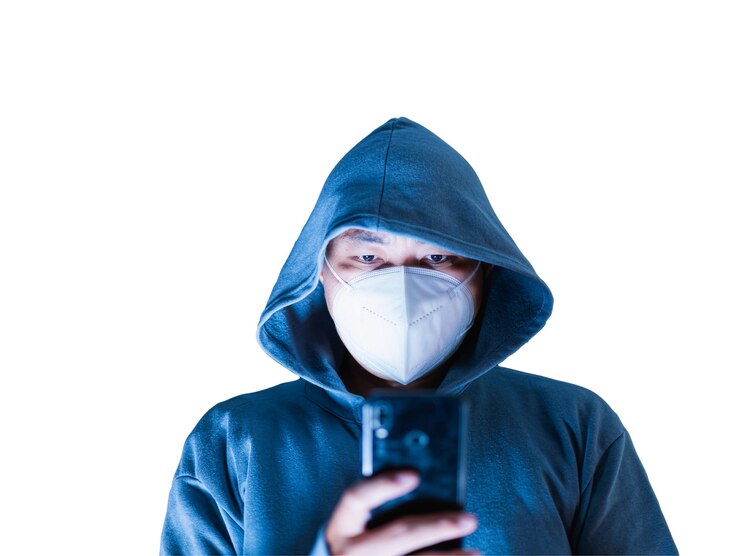 Foto hombre asiático con capucha y máscara hackeando algo de un teléfono móvil destinado a tomar fotos borrosas en un fondo blanco hay una ruta de recorte