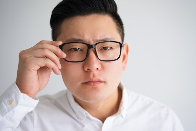 Hombre asiático centrado tratando de ver a través de gafas