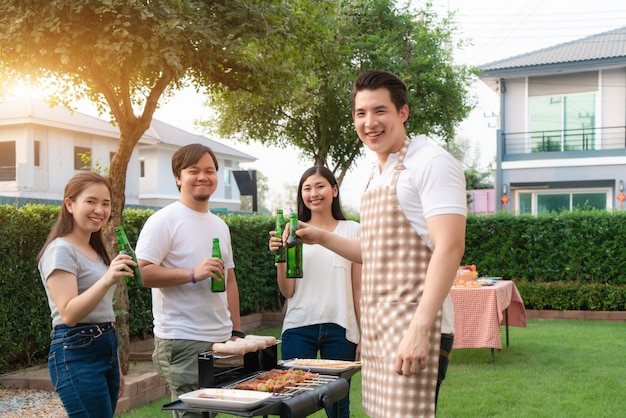 Hombre asiático cocina barbacoa parrilla y salchichas para un grupo de amigos a comer fiesta en el jardín en casa.