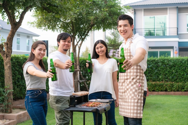 Hombre asiático cocina barbacoa parrilla y salchichas para un grupo de amigos a comer fiesta en el jardín en casa.