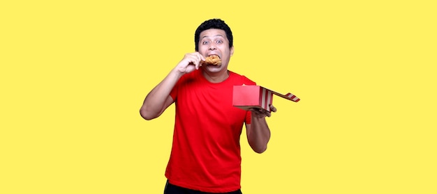 Foto hombre asiático está comiendo pollo frito deliciosamente sobre fondo amarillo