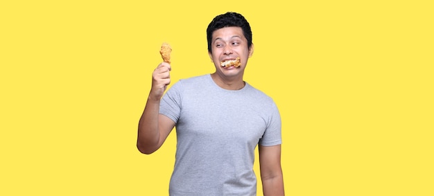 Foto hombre asiático está comiendo pollo frito deliciosamente sobre fondo amarillo