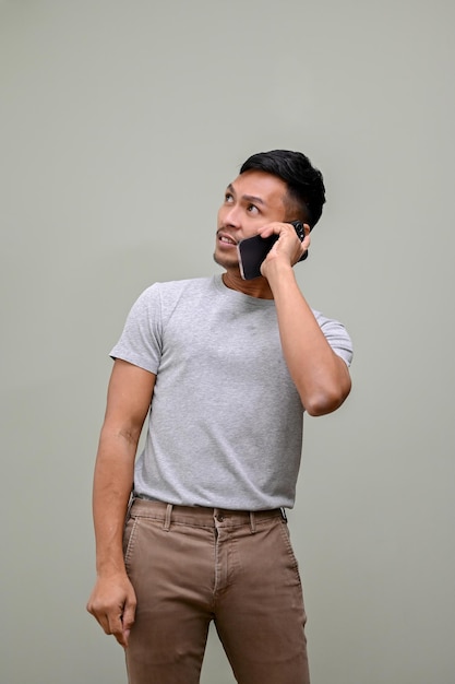 Hombre asiático confundido mirando a un lado o mirando hacia arriba y hablando por teléfono de fondo aislado